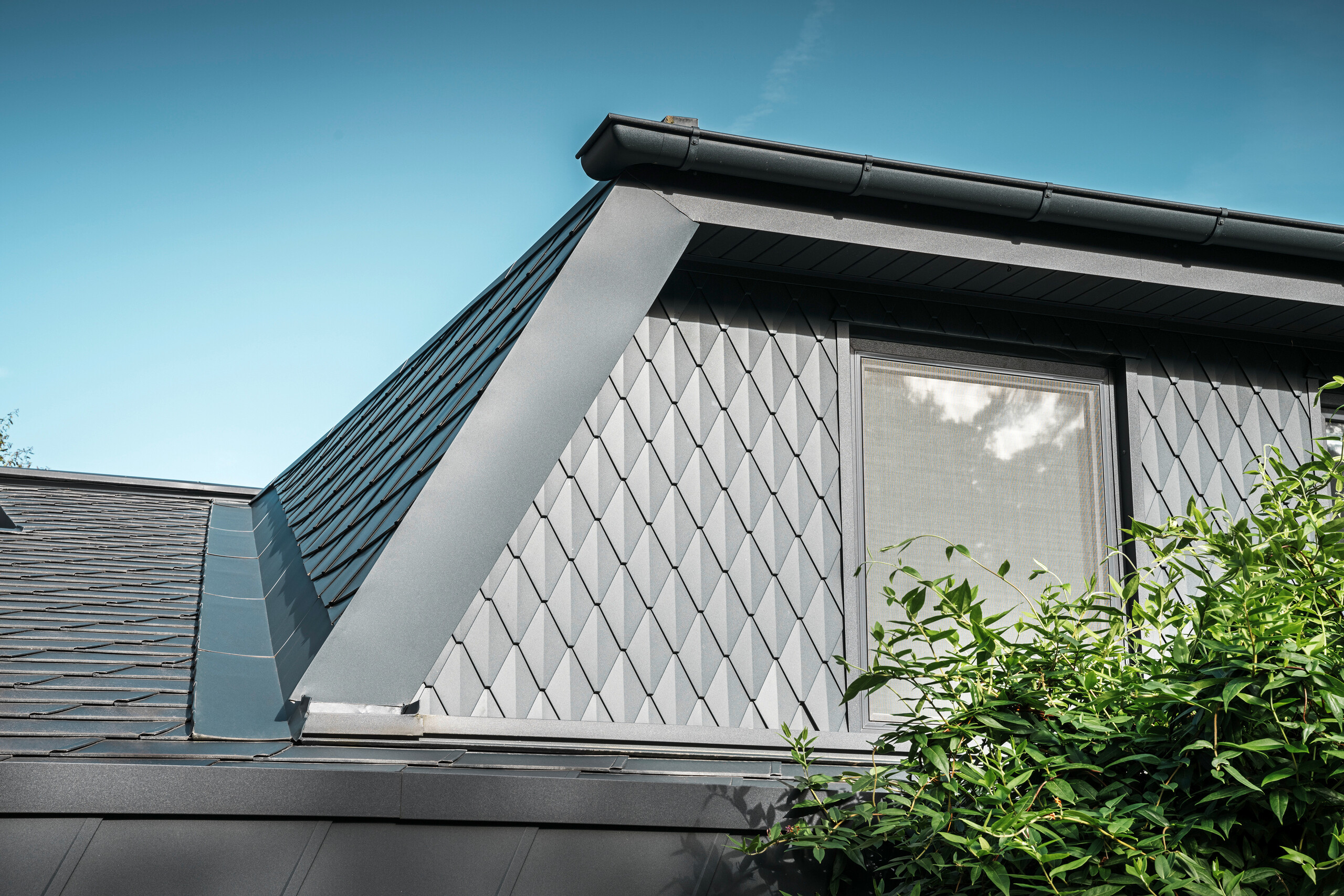 Trapezgaube eines Einfamilienhauses in Mechernich, verkleidet mit kleinen PREFA Dachrauten in P.10 Anthrazit. Das Dach ist mit PREFA Dachschindeln DS.19 in derselben Farbe gedeckt. Die hochwertige Aluminiumverkleidung sorgt für Wetterbeständigkeit und eine moderne, ästhetische Optik.
