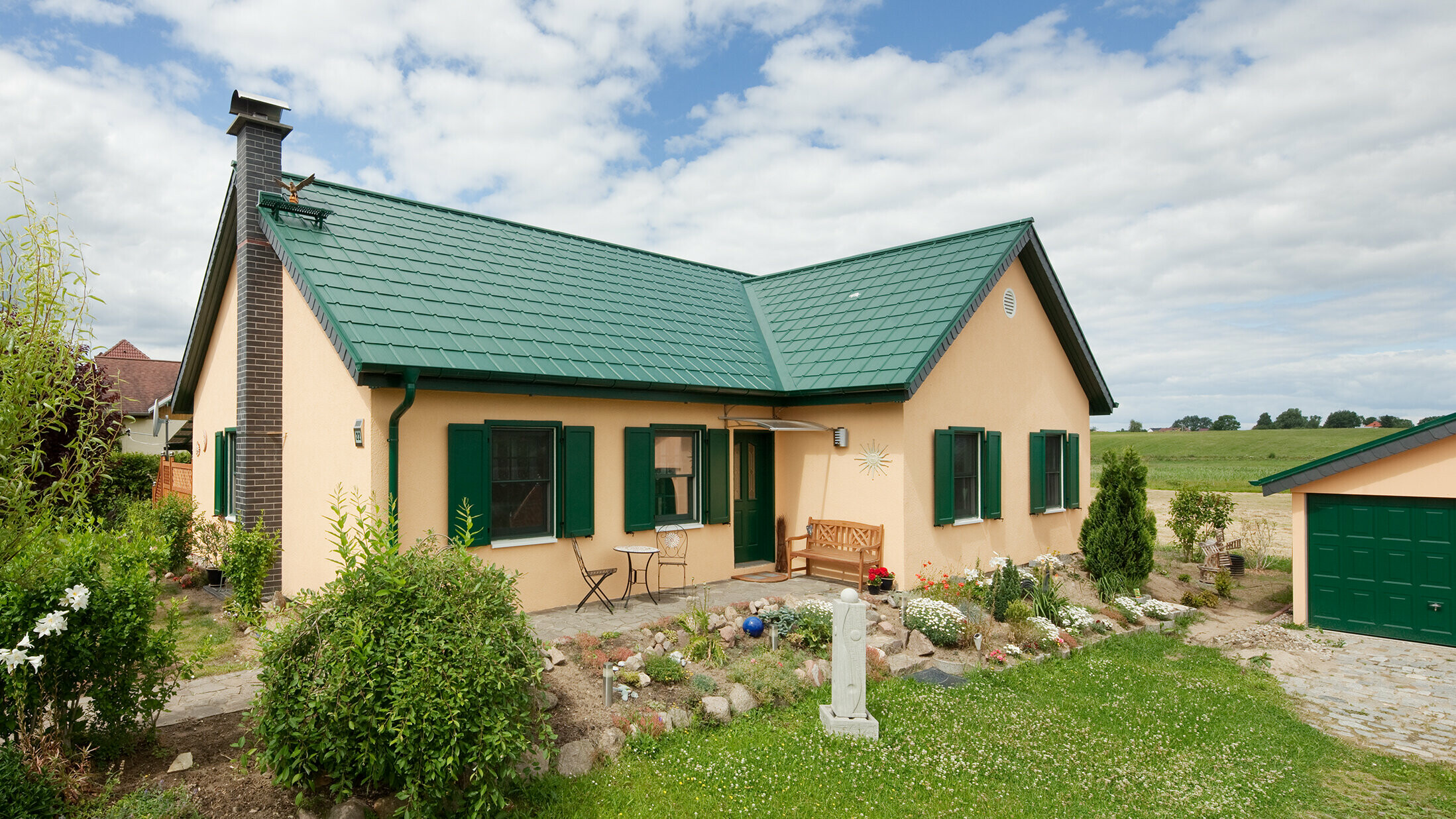 Extended gable roof; L-shaped gable roof; with PREFA roof tiles in P.10 moss green; pretty rural cottage with green shutters to match the PREFA roof.