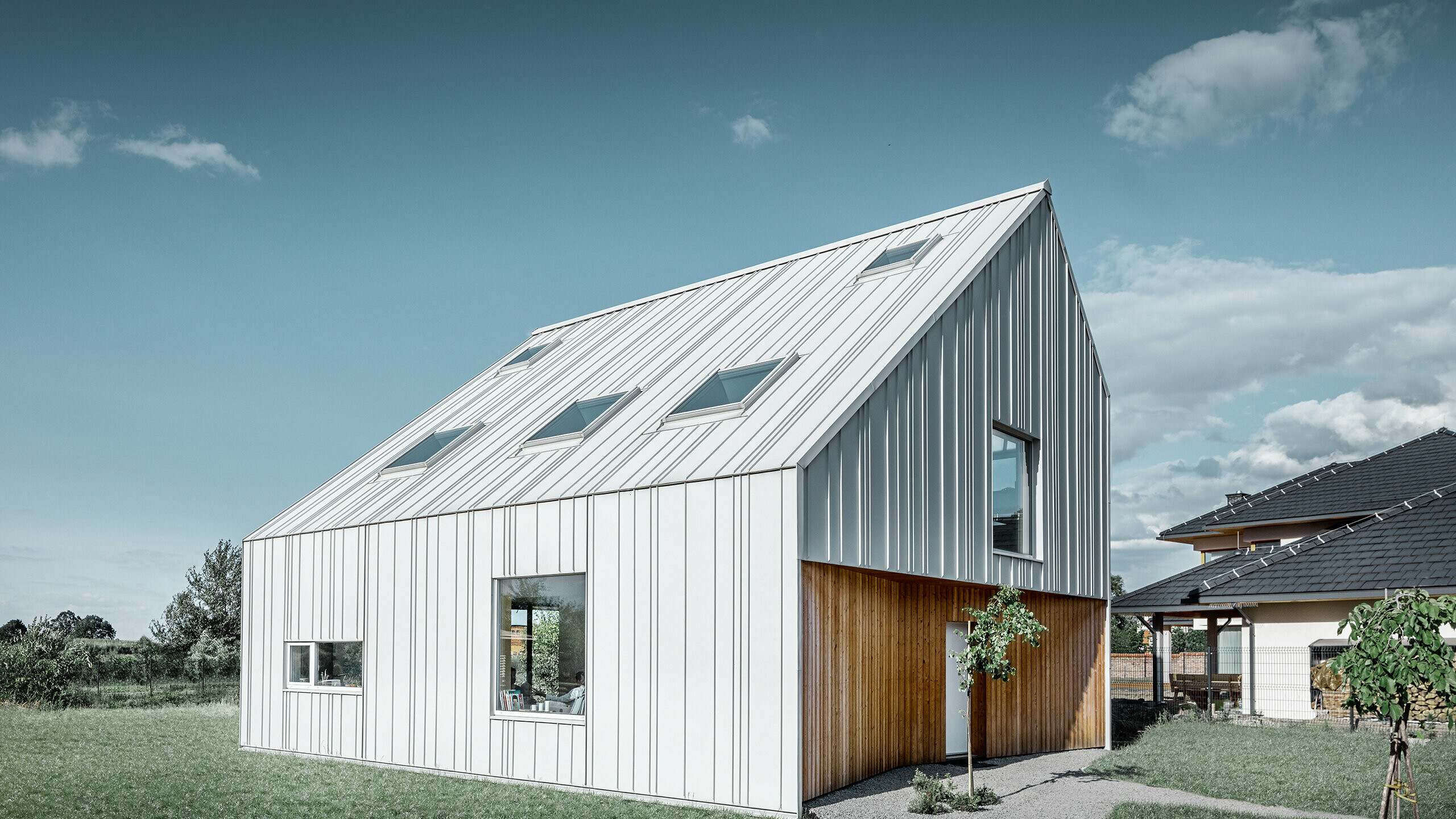 Modern detached house with gable roof, the entire outer skin is clad with PREFALZ standing seam in PREFA white. The panels of different widths extend from the roof over the façade. Several roof windows are installed in the roof.