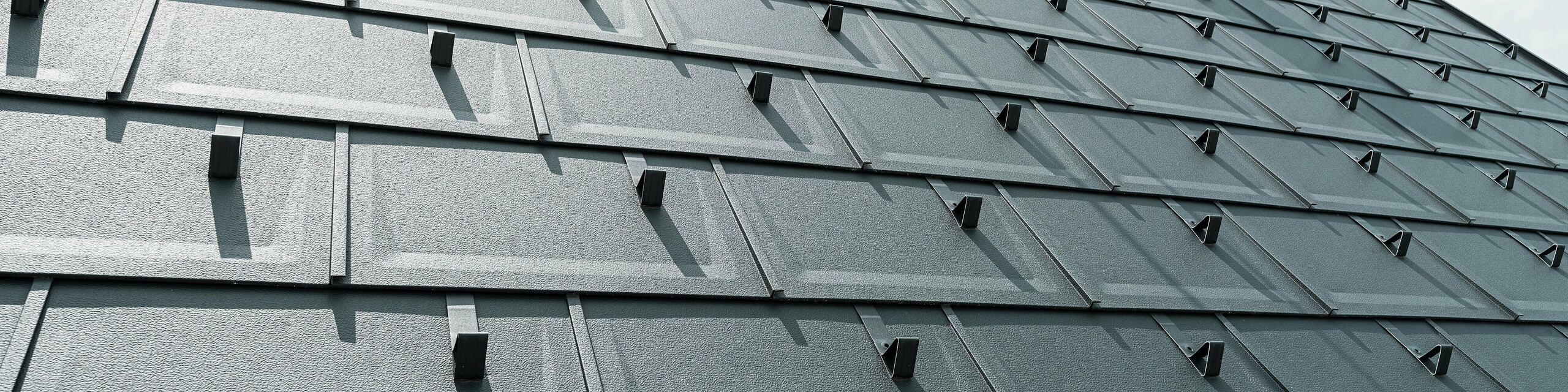 Detailed view of the PREFA R.16 roof tile in colour P.10 anthracite. PREFA snow guards and a smoke hood can be seen on the roof.