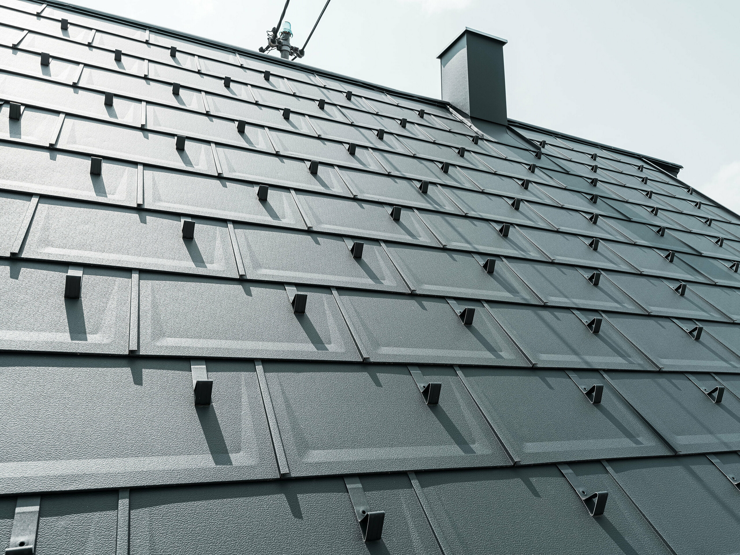 Detailed view of the PREFA R.16 roof tile in colour P.10 anthracite. PREFA snow guards and a smoke hood can be seen on the roof.