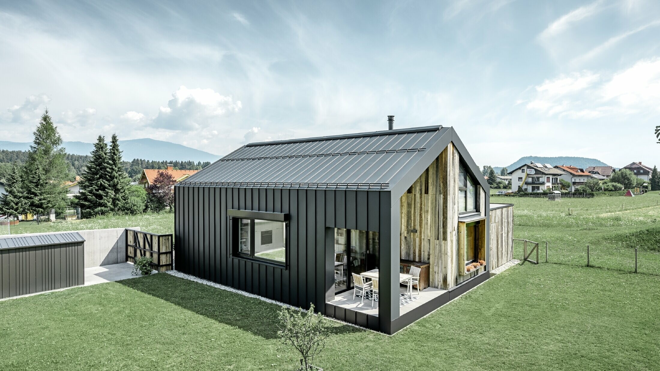 Detached house with gable roof, roof and façade are covered with PREFALZ standing seam from PREFA in P.10 anthracite. The panels of the roof surface extend across the façade. Part of the façade is clad with weathered wood.
