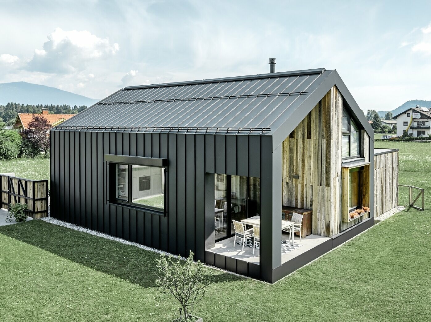Detached house with gable roof, roof and façade are covered with PREFALZ standing seam from PREFA in P.10 anthracite. The panels of the roof surface extend across the façade. Part of the façade is clad with weathered wood.