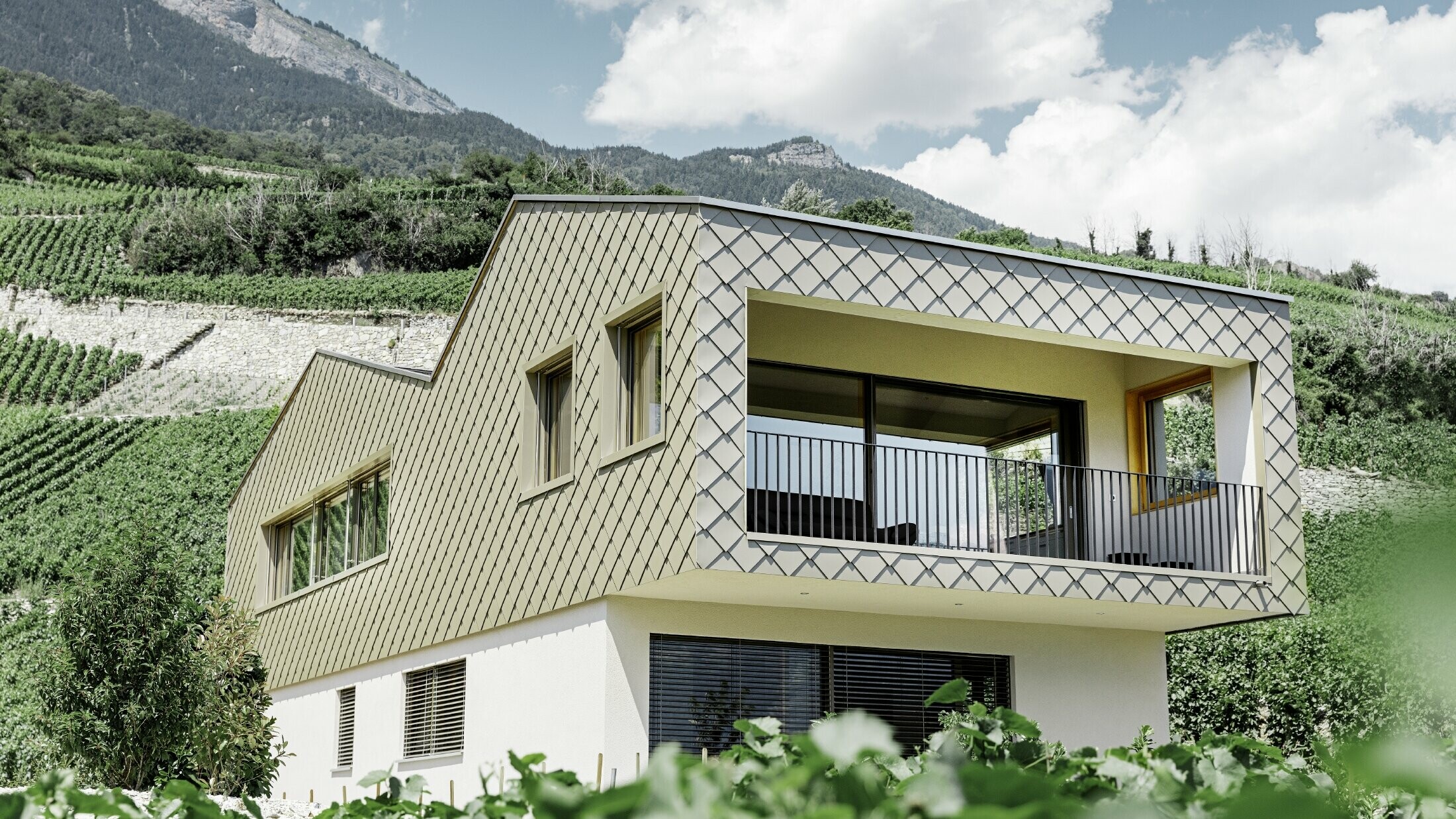 Modern detached house set in the heart of the Rhone valley vineyards with four different roof surfaces and an open gallery clad with rhomboid façade tiles in bronze