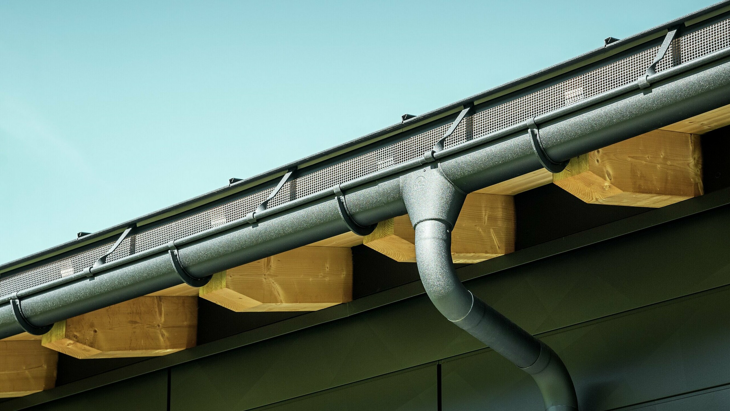 Close-up of the façade of a modern detached house in Ascharina, Switzerland. The sides of the building were clad with striking PREFA Siding.X façade panels in P.10 black. The PREFA roof drainage system with half-round gutter and downpipe is colour-coordinated.