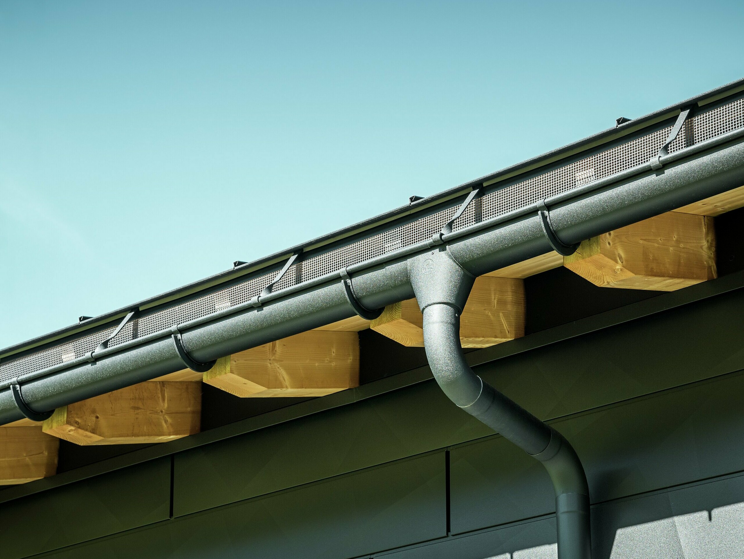 Close-up of the façade of a modern detached house in Ascharina, Switzerland. The sides of the building were clad with striking PREFA Siding.X façade panels in P.10 black. The PREFA roof drainage system with half-round gutter and downpipe is colour-coordinated.