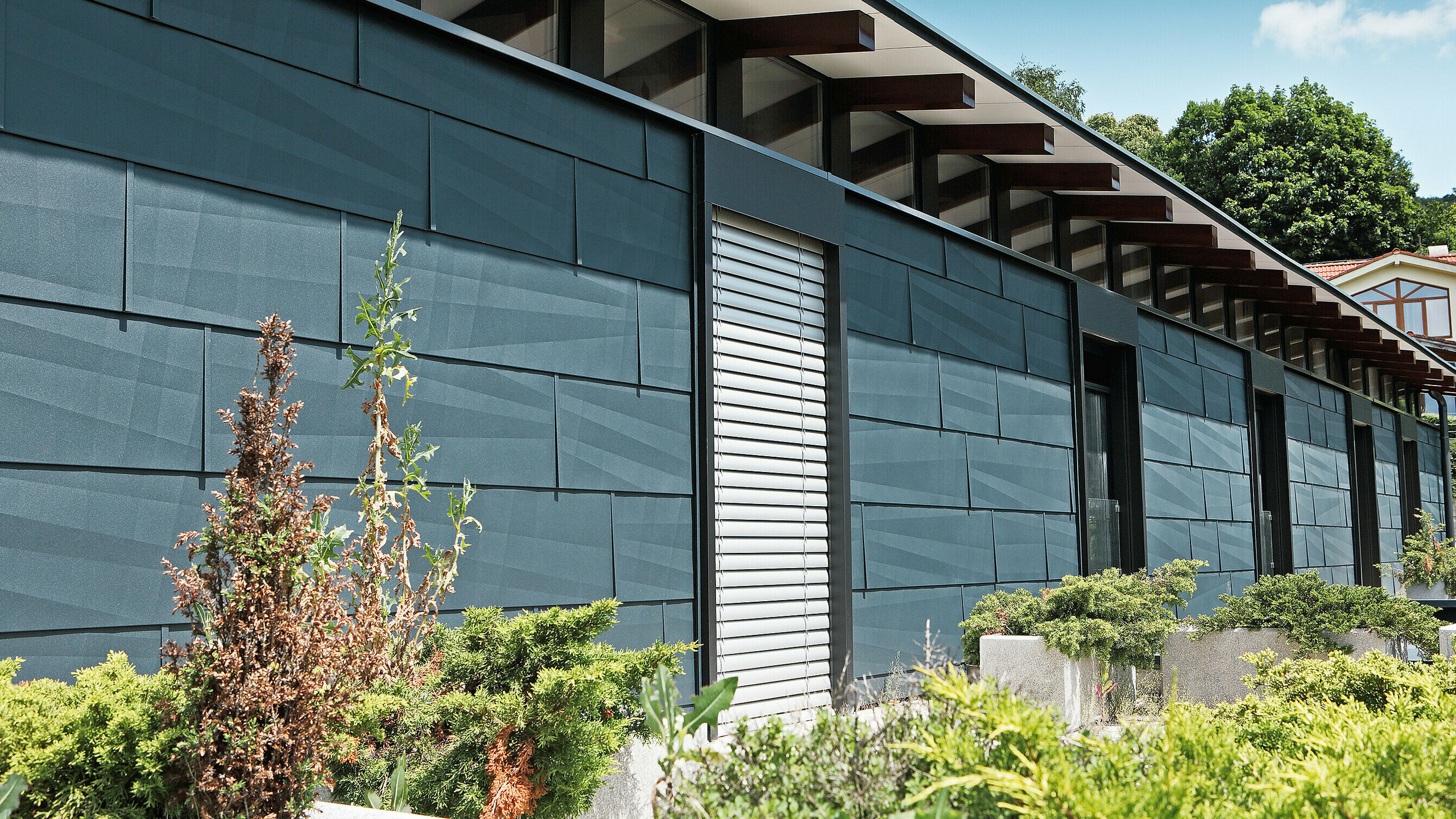 Modern exposed building side designed using FX.12 façade panelling in anthracite, with a garden.