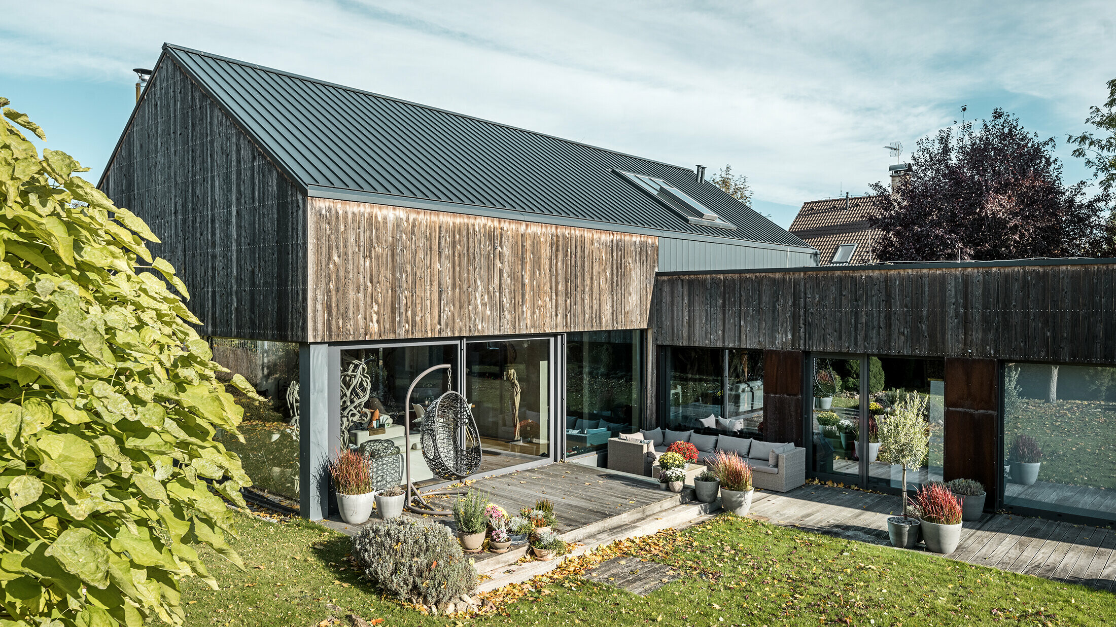 Detached house with gable roof, covered with PREFALZ double standing seam in anthracite and weathered wooden façade. With a beautiful wooden terrace and large windows on the ground floor.