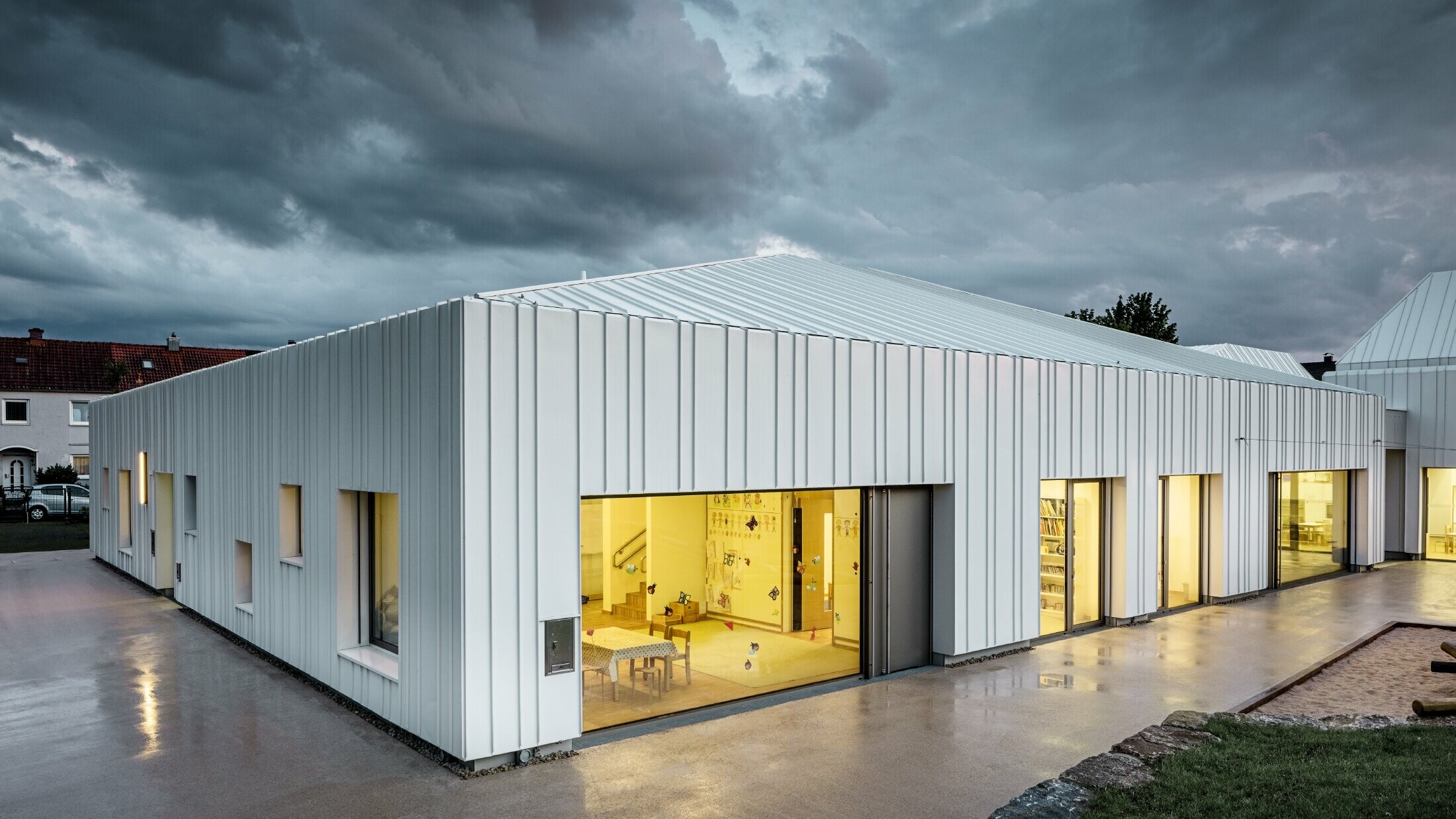 Day nursery in Niederwerrn with PREFALZ standing seam roof and façade in pure white with different widths of panels photographed at dusk and in a cloudy atmosphere