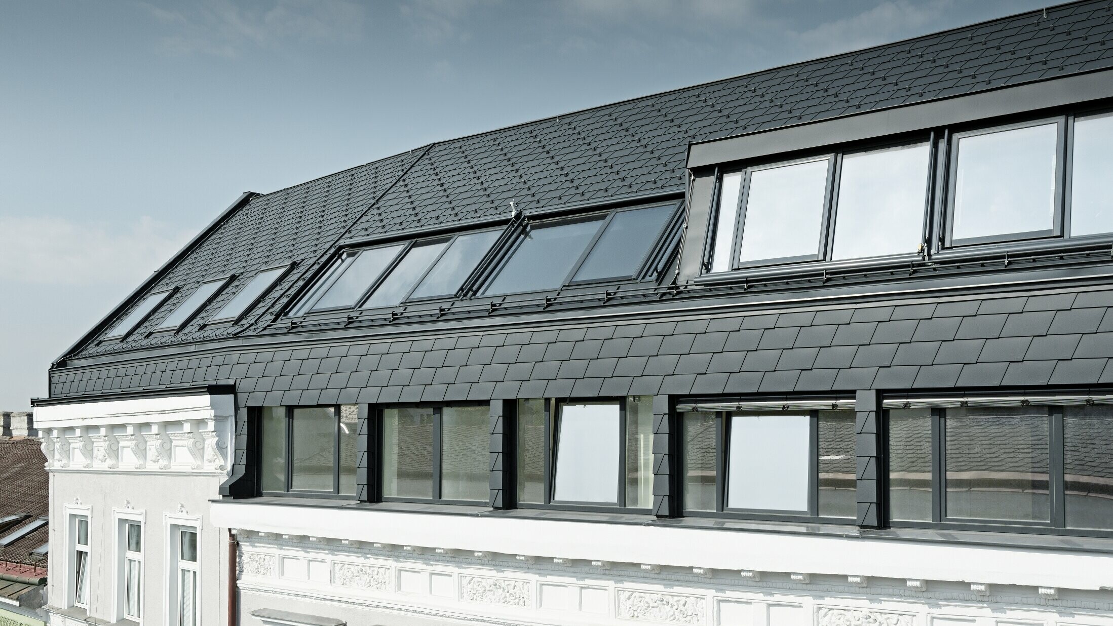 Extended roof conversion of a residential complex in Mariahilferstraße, Vienna; covered with PREFA roof shingles and façade shingles in anthracite P.10.