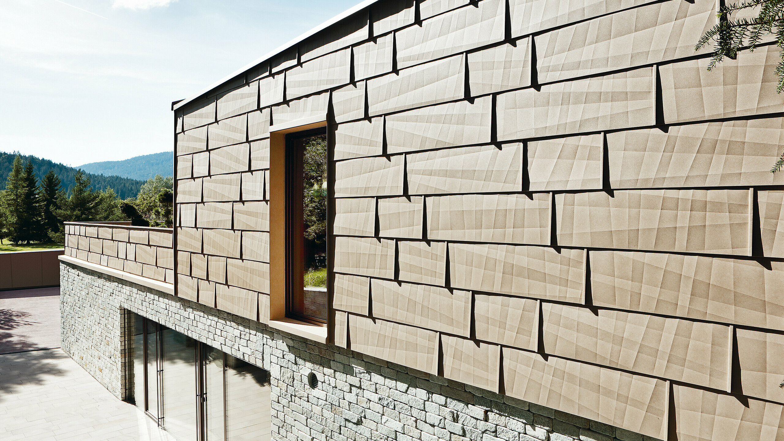 On this external façade, the PREFA FX.12 façade panel in P.10 sand brown has been combined with a stone façade on the bottom floor.