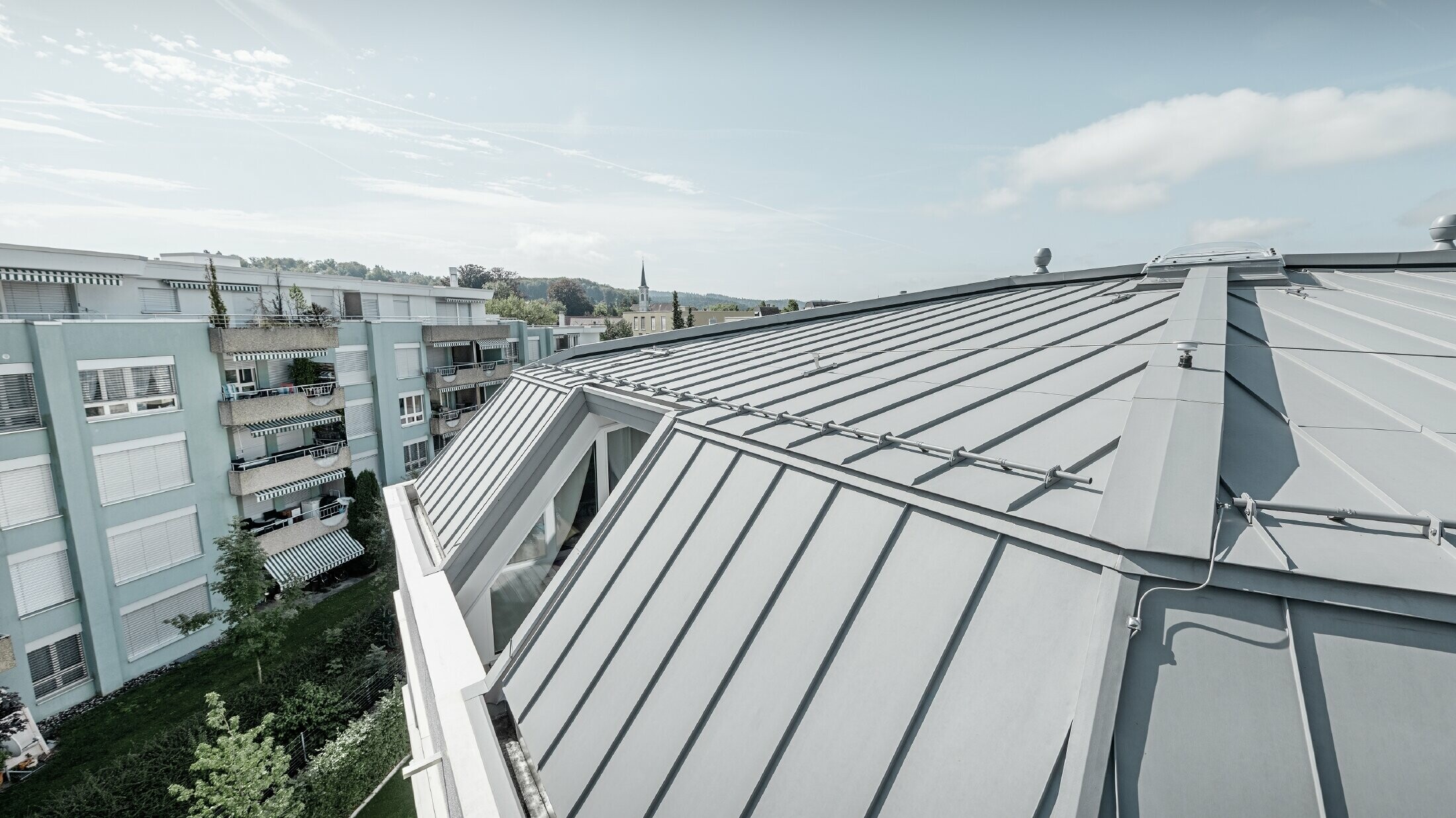 Close up of the roof area of an apartment building. Standing seam roof designed with PREFA Prefalz in patina grey.