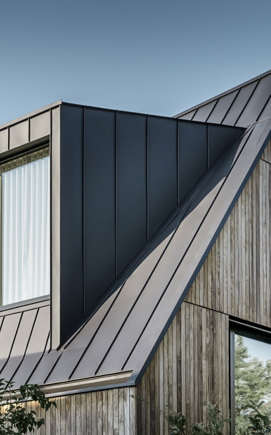 Steep gable roof with large dormer, covered with PREFALZ by PREFA in anthracite standing seam roof combined with wooden façade